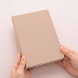 Hands holding tsuki constellations bullet journal in soft moondust beige