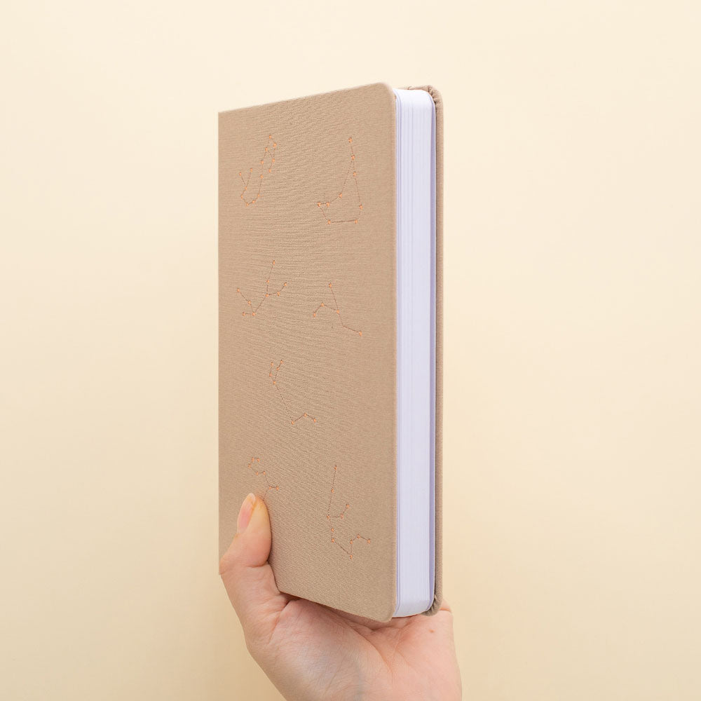 Hand holding beige bullet journal with constellations design in rose gold foil 