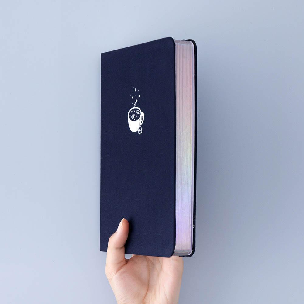 Tsuki ‘Cup of Galaxy’ Limited Edition Holographic Bullet Journal held in hand at spine angle in light blue background
