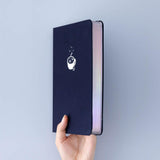 Tsuki ‘Cup of Galaxy’ Limited Edition Holographic Bullet Journal held in hand at spine angle in light blue background