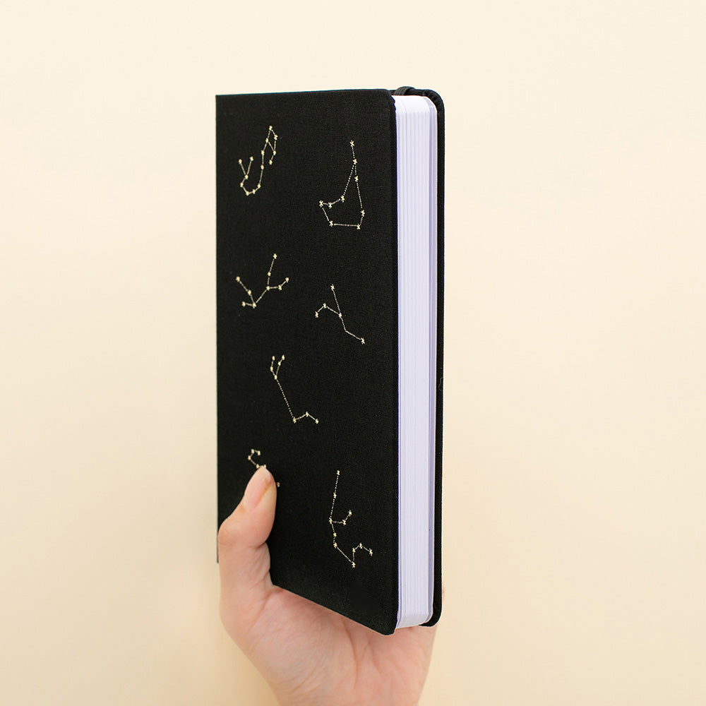 Hand holding black bullet journal with constellations design in gold foil 