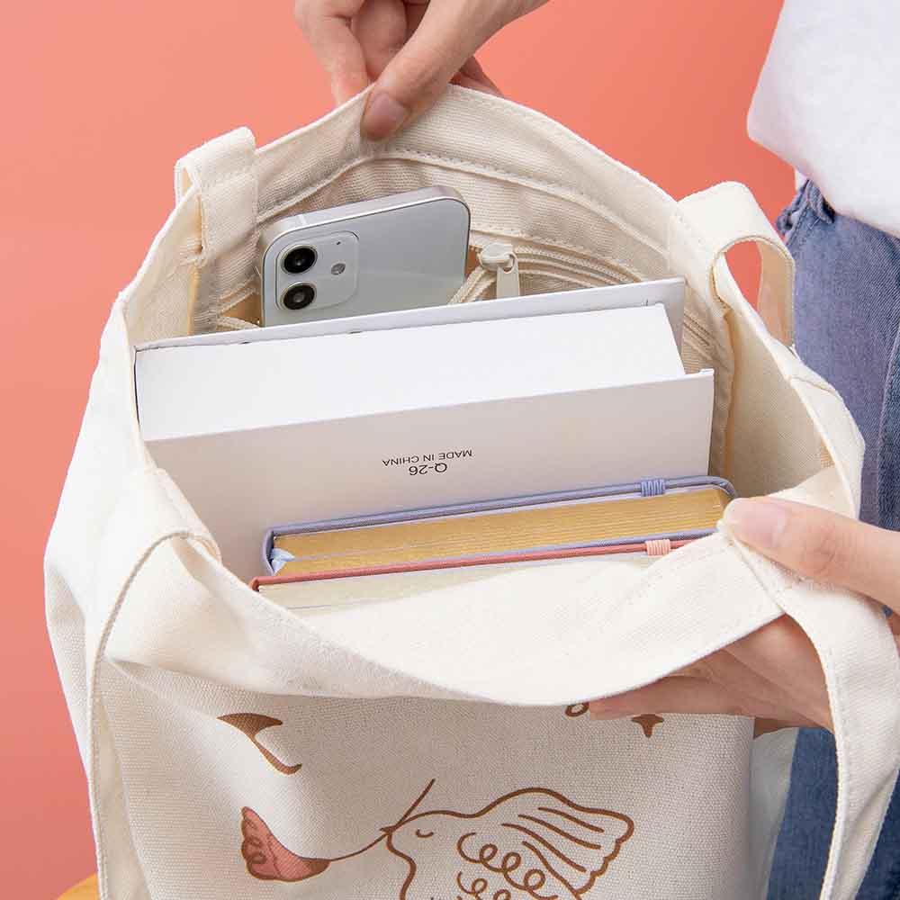 Tsuki ‘Moonflower’ Limited Edition Tote Bag with ‘Suzume’ Limited Edition Bullet Journal and ‘Full Bloom’ Limited Edition notebook inside held in hands on coral pink background