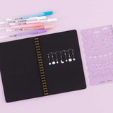 Open Tsuki Black Paper Ringbound Bullet Journal with Gelly Roll Pens and Tsuki Bullet Journal Stencil Set in Lilac Taro on lilac background