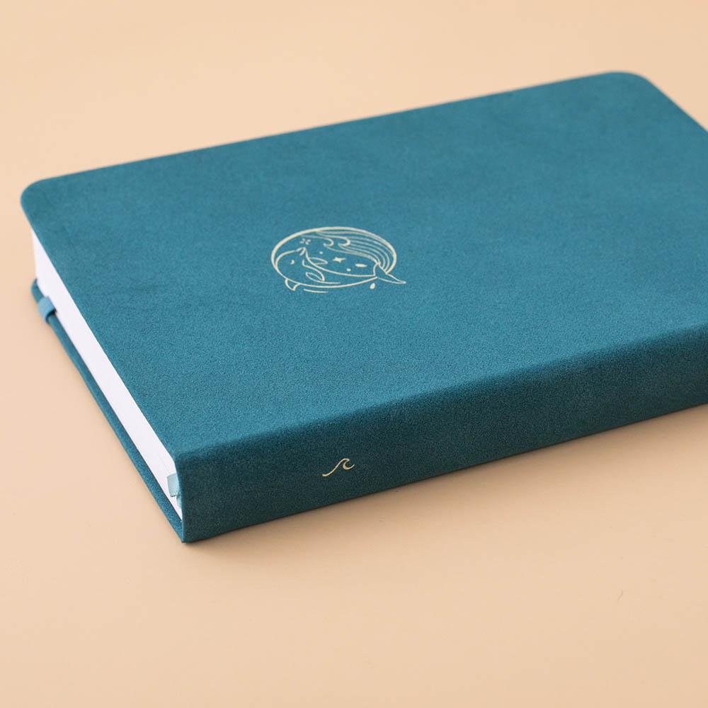 Close up of the front cover and spine of Sea green velvet Tsuki Dolphin Days bullet journal on peach background