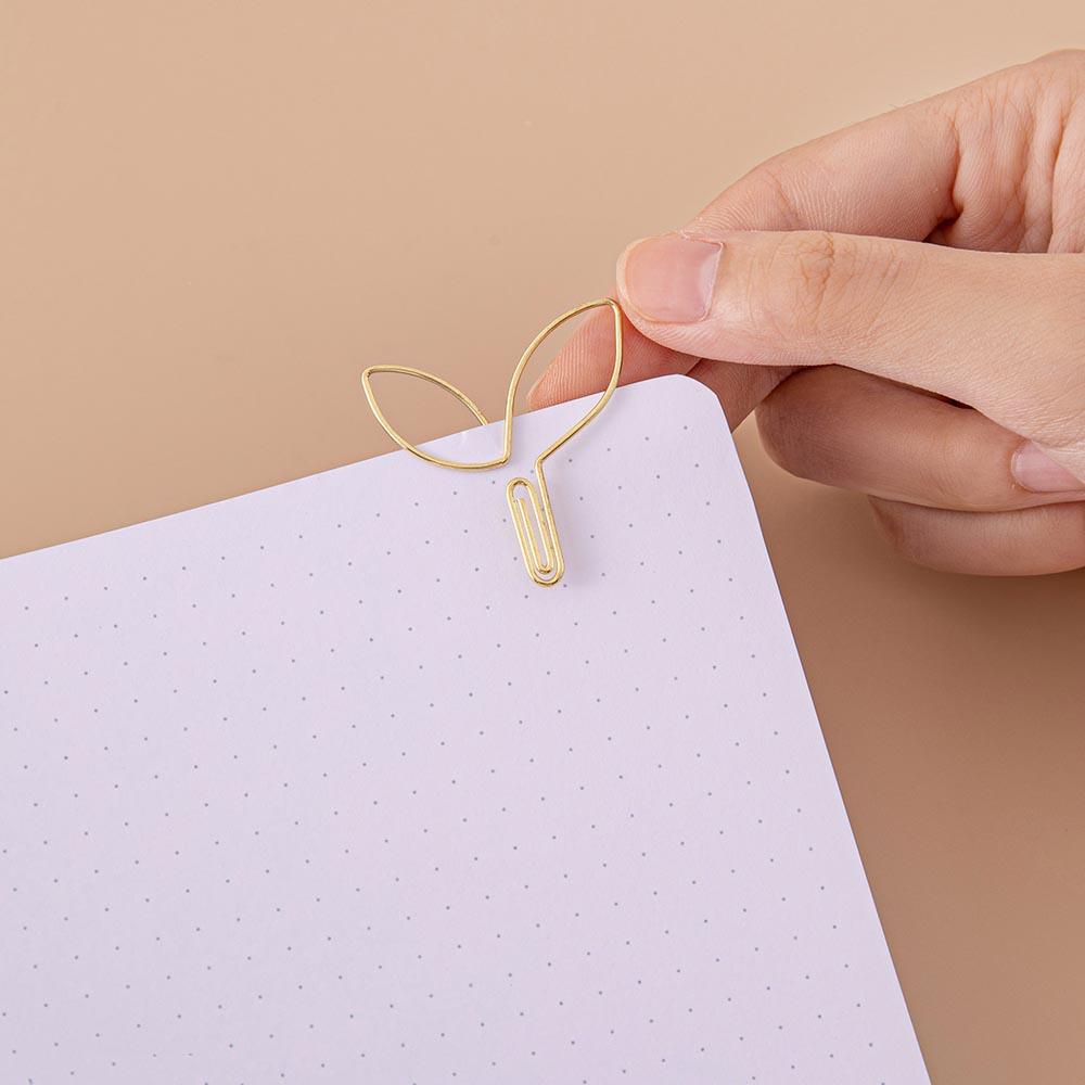 Close up of open page of Tsuki ‘Midnight Garden’ Limited Edition Bullet Journal held in hand with free paperclip gift on beige background