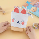 Tsuki ‘Four Seasons’ Embroidered Pop-Up Pencil Case by Notebook Therapy x Milkkoyo in kitty held in hands with Tsuki ‘Four Seasons’ Bullet Journal Stamps and Tsuki ‘Four Seasons’ Washi Tapes and Tsuki ‘Four Seasons: Autumn Edition’ Bullet Journal on honey yellow background