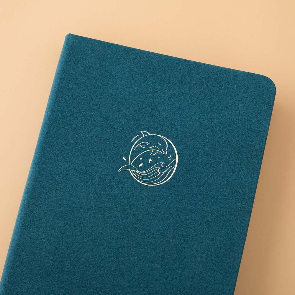 Close up of the front cover of Sea green velvet Tsuki Dolphin Days bullet journal on peach background