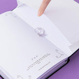 Close up of open back page pocket of Tsuki ‘Moonlit Spell’ Limited Edition Holographic Bullet Journal with free bookmark gift held in hand on purple background