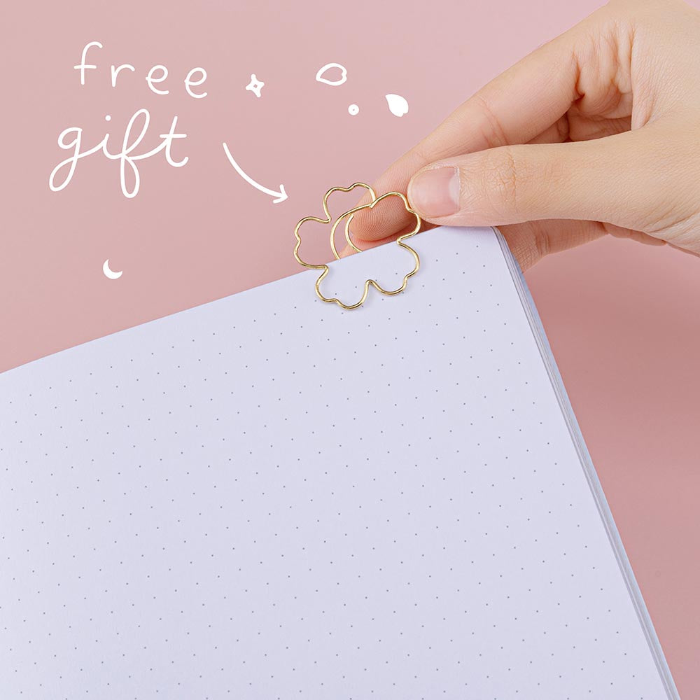 Close up of open Tsuki ‘Sakura Journey’ Limited Edition Bullet Journal with free bookmark gift held in hand in pink background