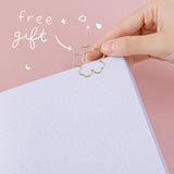 Close up of open Tsuki ‘Sakura Journey’ Limited Edition Bullet Journal with free bookmark gift held in hand in pink background