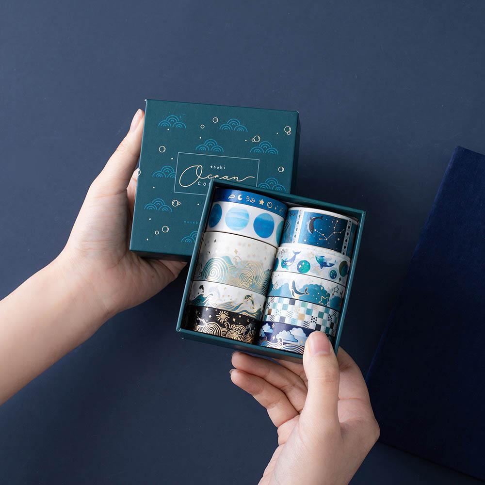 Tsuki Ocean Edition Washi Tapes and sticker sheet set with reusable eco-friendly gift box held in hands in dark blue background