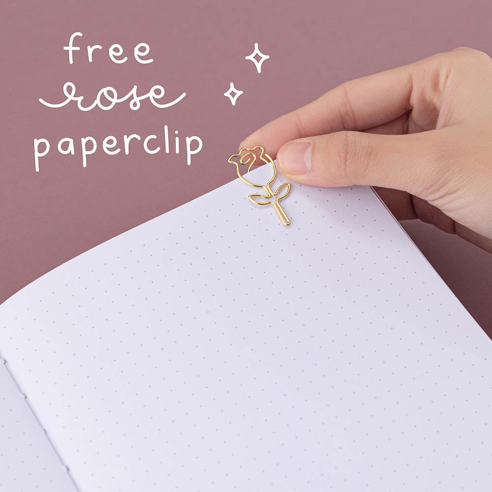 Close up of open Tsuki ‘Vintage Rose’ Limited Edition Bullet Journal with free rose paperclip held in hand in mauve background