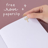 Close up of open Tsuki ‘Vintage Rose’ Limited Edition Bullet Journal with free rose paperclip held in hand in mauve background