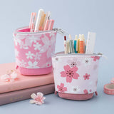 Tsuki 'Sakura Edition' Pop-Up Pencil Case in blush pink and petal pink with pens inside on Tsuki 'Sakura' Limited Edition Bullet Journal in Blush Pink and Petal Pink with sakura flowers in light blue background