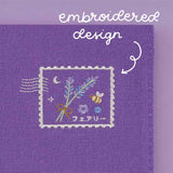 Close up of embroidered design at the back of the notebook pouch featuring lavender, bee, crescent moon and some Japanese text in a stamp shape