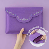 Hand holding a purple fabric notebook envelope pouch with flower embroidery and an image in the middle of a notebook fitting in the envelope notebook pouch
