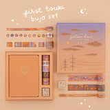 Flatlay of an opened Tsuki Golden Hour Bullet Journal Box Set contents of box includes an orange linen notebook, 6x washi tapes and 1x wooden rubber stamp