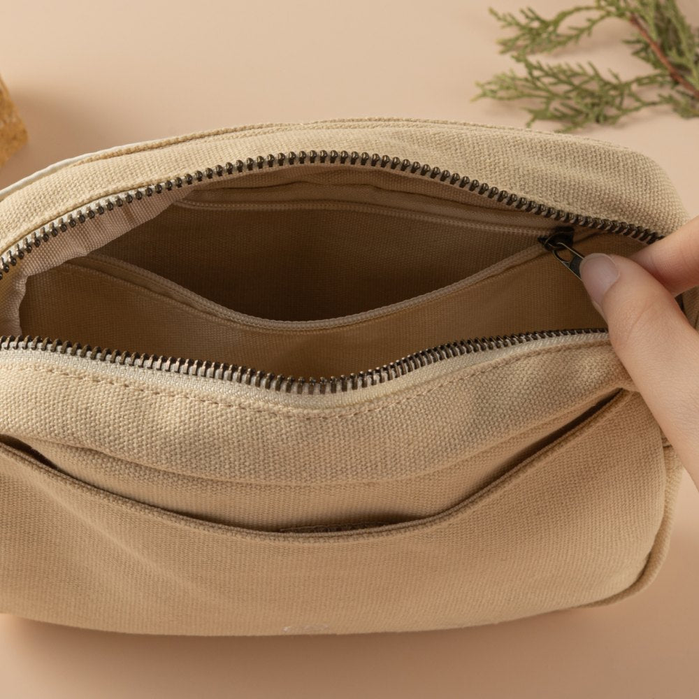 Hand unzipping the inside pocket of the Hinoki cream canvas travel pouch