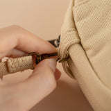 Hand unhooking the strap from hinoki cream canvas travel pouch