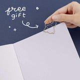 Close up of open page of Tsuki ‘Suzume’ Winter Limited Edition Bullet Journal with free bookmark gift held in hand on navy background