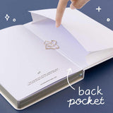 Open back page pocket of Tsuki ‘Suzume’ Winter Limited Edition Bullet Journal held in hand with free bookmark gift on navy background