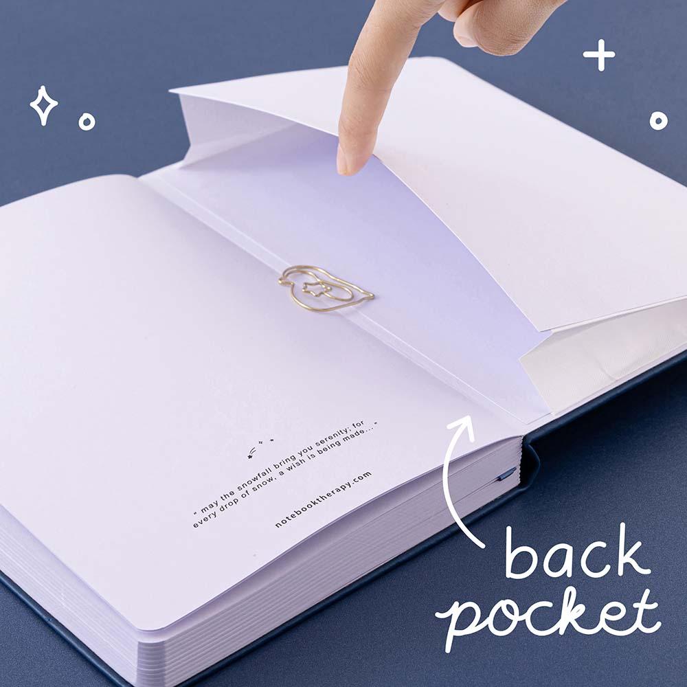 Open back page pocket of Tsuki ‘Winter Wishes’ Limited Edition Bullet Journal held in hand with fere paperclip gift on navy background