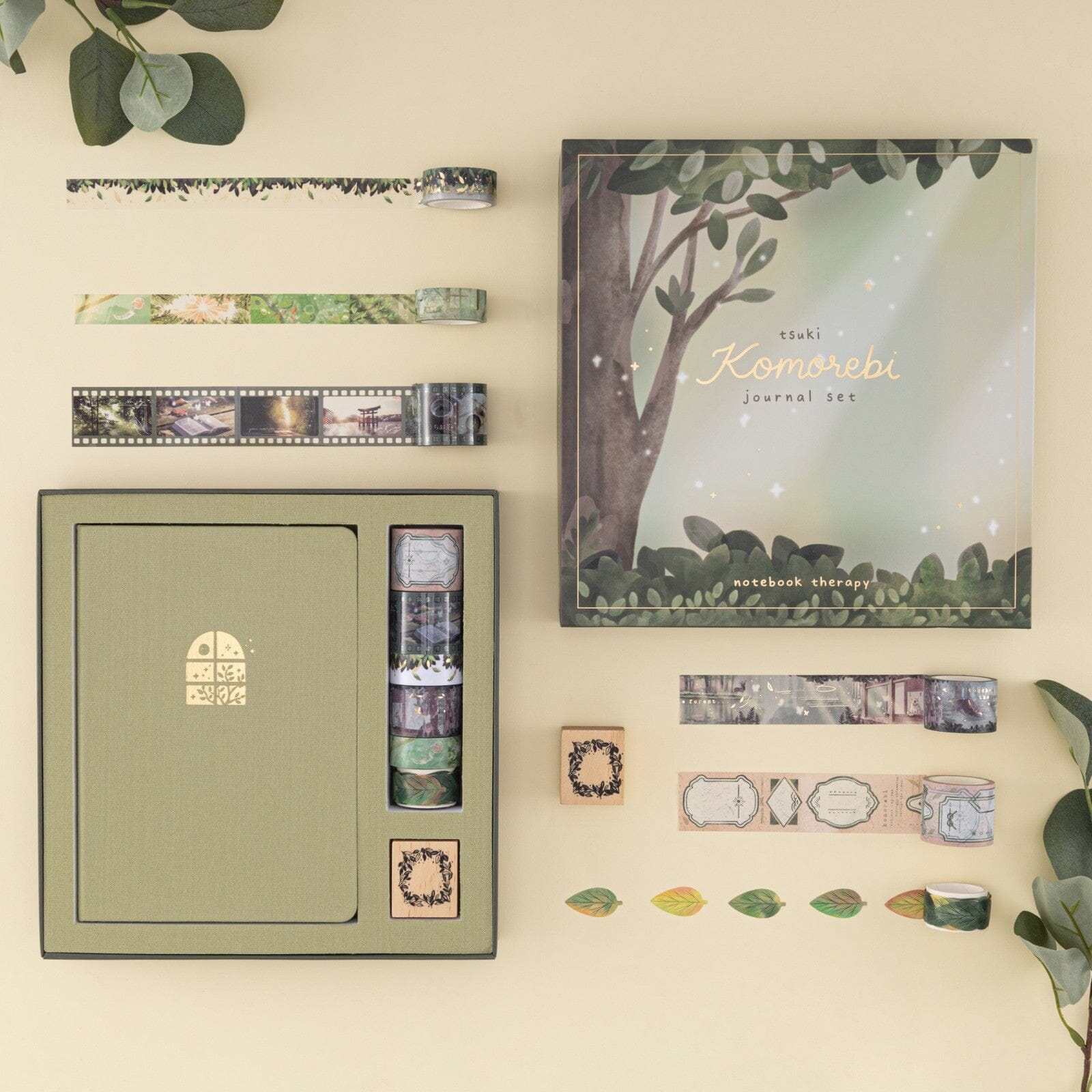 Flatlay of Tsuki ‘Komorebi’ journal set, opened box with 6x washi tapes, green linen bullet journal and a wreath border rubber stamp