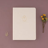 Bullet Journal notebook with gold key illustrated detail on the cover on linen with heart-shaped padlock paperclip and dried flowers on the side