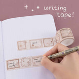 Tsuki ‘Vintage Rose’ Writing Washi Tape rolled out on Tsuki ‘Vintage Rose’ Limited Edition Bullet Journal with pen held in hand on mauve background