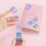 Tsuki ‘Sakura Journey’ Vintage Journal Stamp Washi held in hands over Tsuki ‘Sakura Journey’ Limited Edition Travel Notebook on pink background
