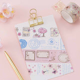 Tsuki ‘Sakura Journey’ Vintage Journal Washi Tape Set on white clipboard with gold pen and cherry blossoms on pink background