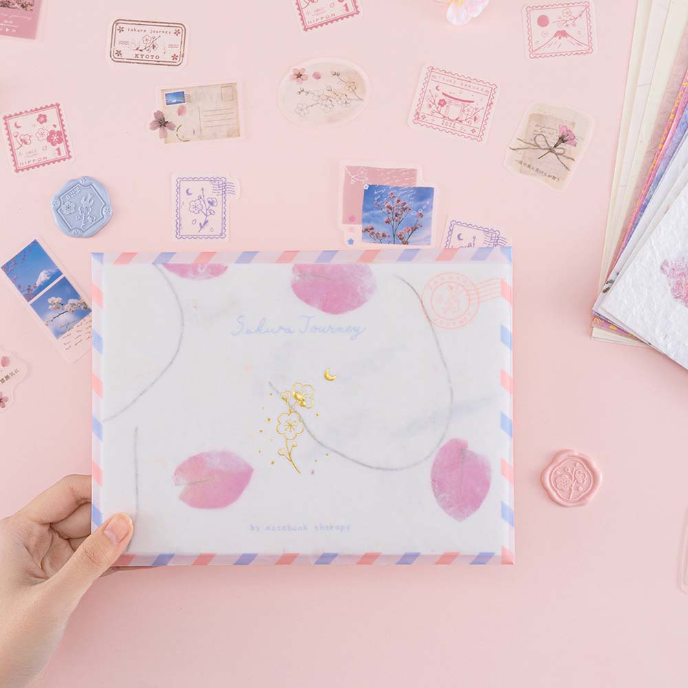 Tsuki ‘Sakura Journey’ Scrapbooking Set on envelope held in hand on pink background