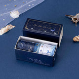 Open box of ocean-themed washi tape on a blue background with seashells scattered around it