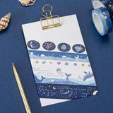 Swatch of the tsuki Gentle Giant washi tape set on white paper against a blue background + gold pen and  seashells for decoration