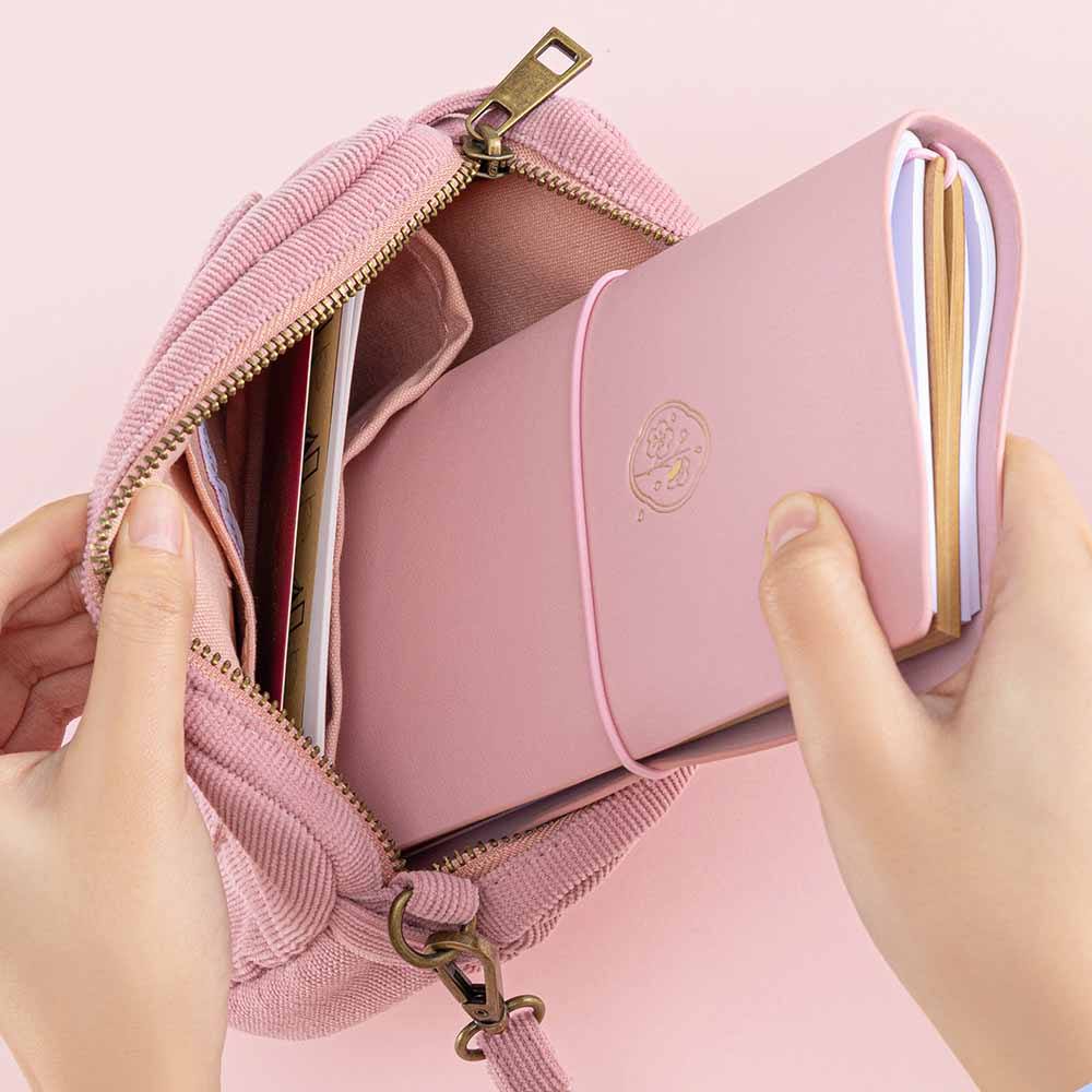 Tsuki ‘Sakura Journey’ Travel Pouch held in hands with Tsuki ‘Sakura Journey’ Limited Edition Travel Notebook inside in pink background