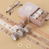 Tsuki Light Academia Washi Tape Set by Notebook Therapy on brown background with a pair of glasses and some pressed daisies around the open box and washi tape rolls