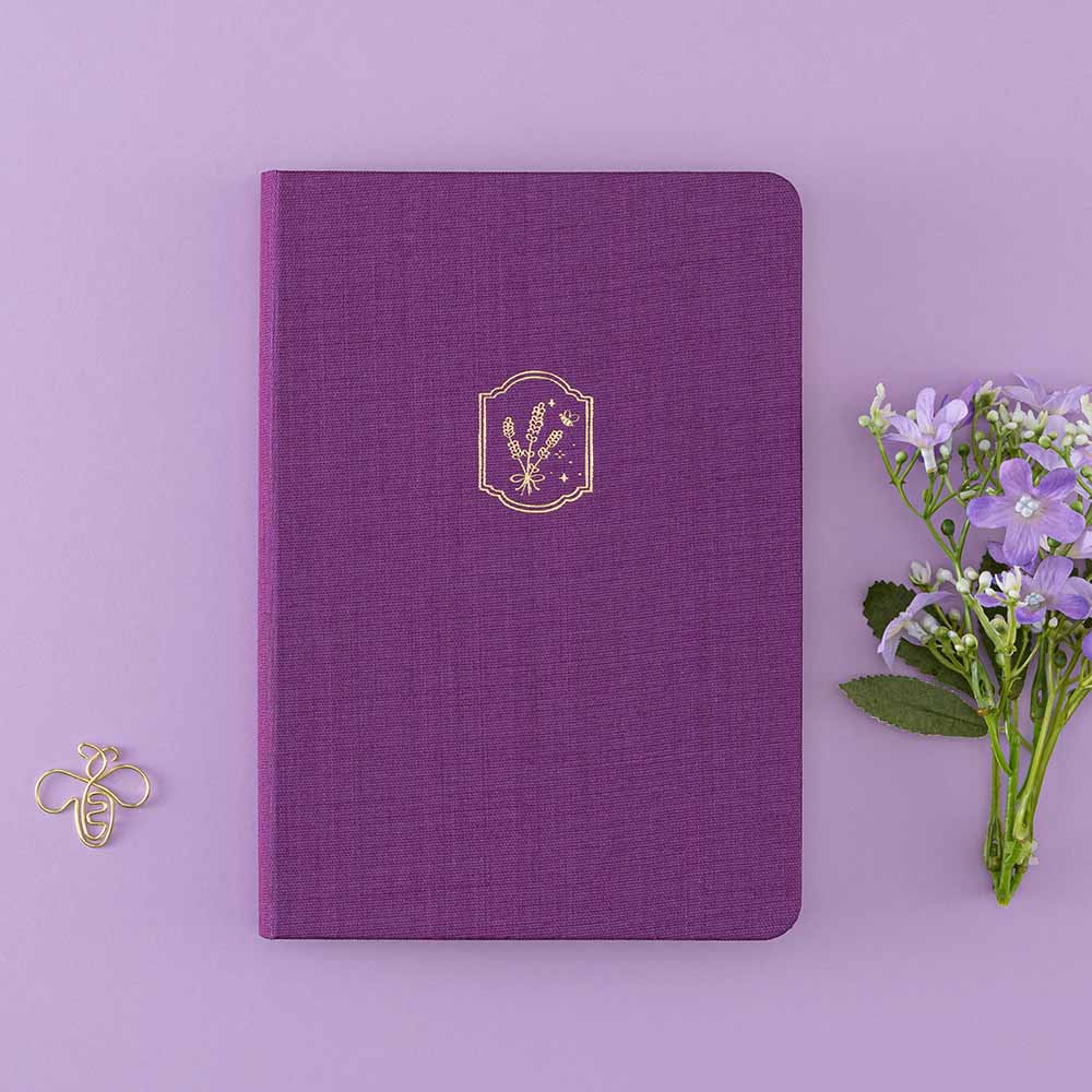 Tsuki ‘Enchanted Garden’ lavender foil design on purple linen bullet journal on purple background with bee shaped paper clip and purple flower