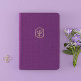 Tsuki ‘Enchanted Garden’ lavender foil design on purple linen bullet journal on purple background with bee shaped paper clip and purple flower