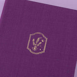 Tsuki ‘Enchanted Garden’ lavender foil design on purple linen bullet journal on purple background close up shot