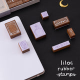 Tsuki ‘Moonlit Alchemy’ stamps on black background exposing the rubber material under some of the stamps and a text that reads “lliac rubber stamps”