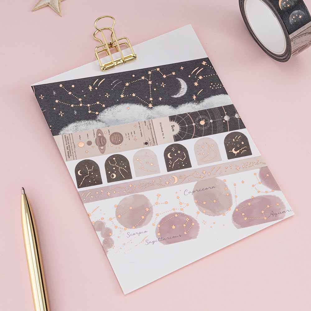 Constellations washi tape rolls swatched on white card with gold clip and a gold pen next to it on a pink background