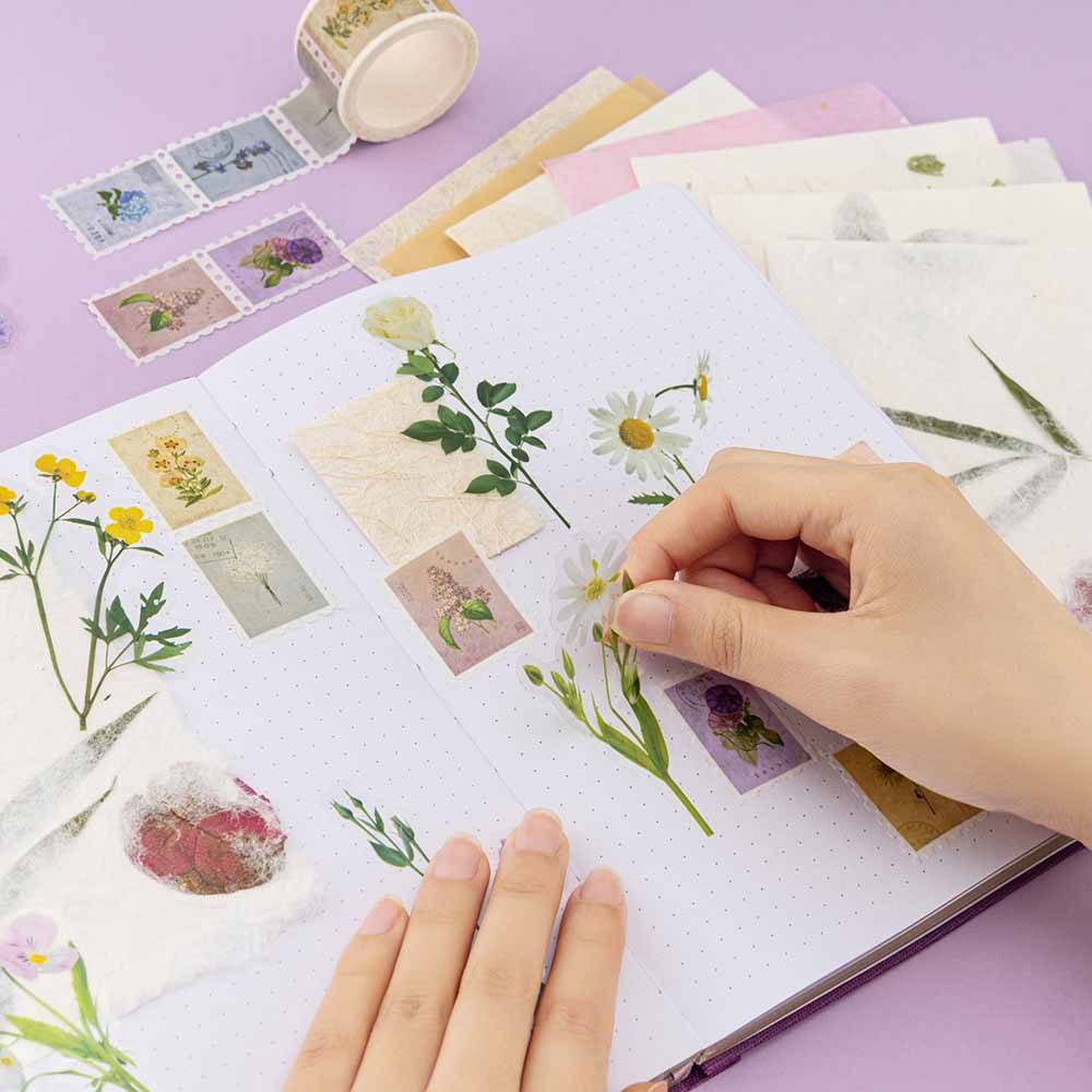 Hand sicking a daisy flower sticker on a bullet journal with flower stickers all over the page