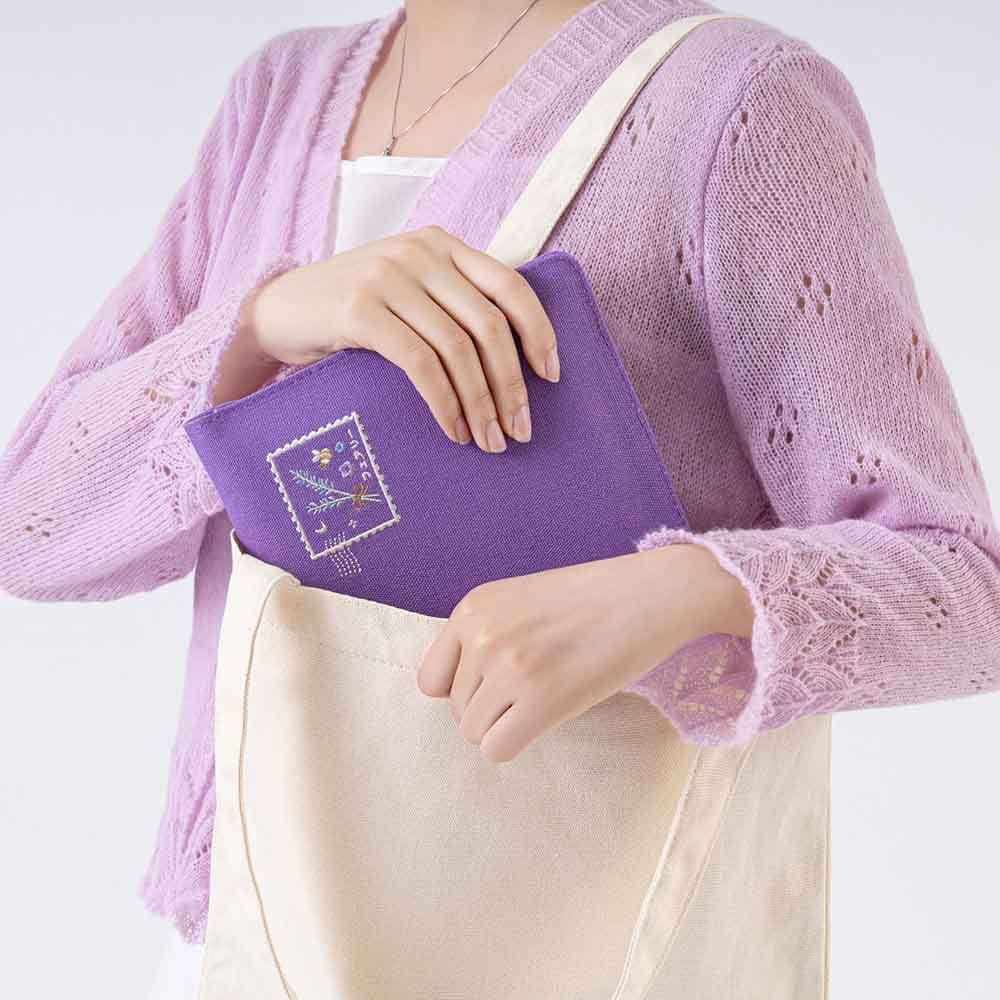 Hand holding the notebook pouch and putting it in a canvas tote bag