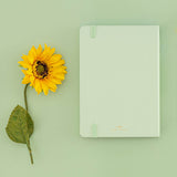Back of Tsuki Four Seasons Summer Collectors Edition 2022 sage bullet journal notebook next to a sunflower on a sage green background