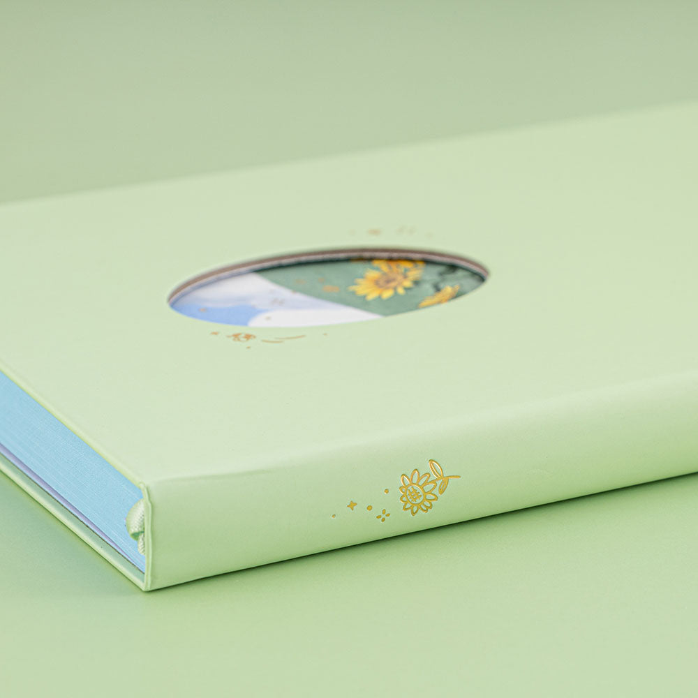 Angled photo of Tsuki Four Seasons Summer Collectors Edition 2022 sage bullet journal notebook showing the gold foil sunflower details on the spine