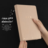 Hands holding Tsuki Stardust Dawn Bullet Journal showing rose gold details