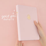 Hand holding Tsuki Sakura Breeze limited edition bullet journal by Notebook Therapy at an angle showing gold foil details