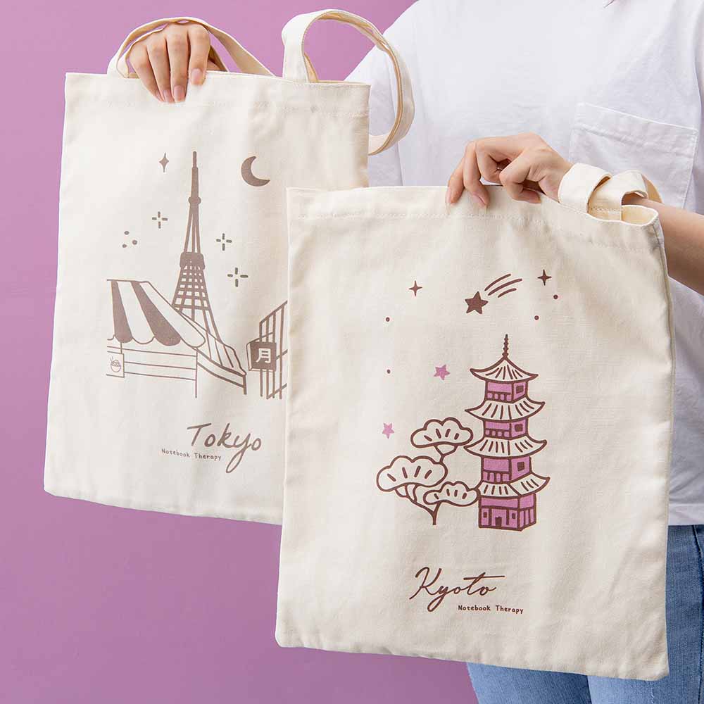 Hands holding up two canvas tote bags, one that says Tokyo and one that says Kyoto