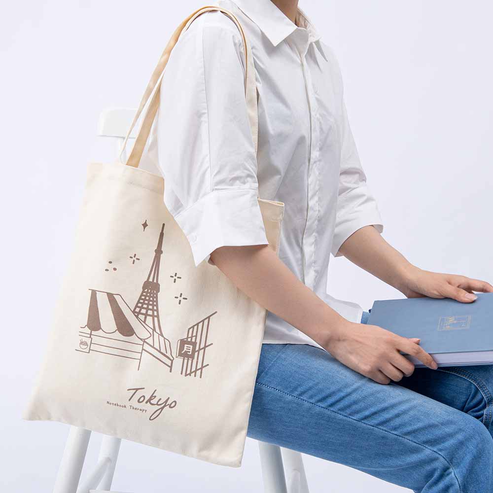 Woman carrying a Tokyo tote bag and a blue notebook