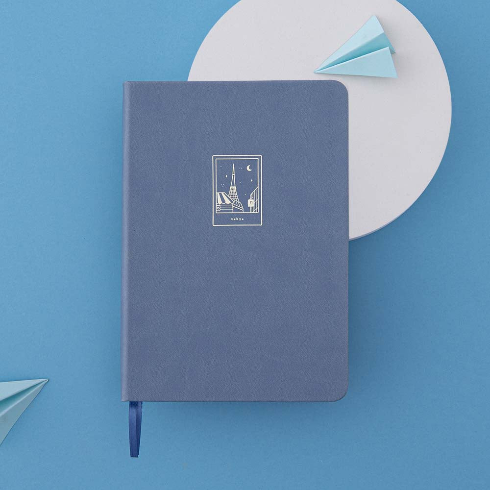 Flatlay of Tsuki Tokyo bullet journal with stone blue leather cover with gold details against a blue background